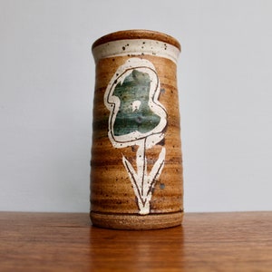 May include: A brown ceramic vase with a white and green stylized flower design.