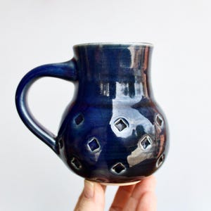 May include: A dark blue ceramic mug with a rounded body and a handle. The mug has a textured surface with a pattern of small, diamond-shaped cutouts.