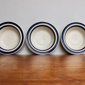 May include: Three white ceramic bowls with blue and white stripes around the rim. The bowls are arranged in a row on a wooden surface.