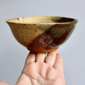 May include: A small, hand-thrown ceramic bowl with a speckled brown and tan glaze on the outside and a darker brown glaze on the inside.