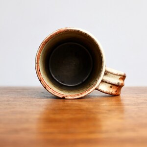 May include: A ceramic mug with a white glaze and brown and orange speckles. The mug has a rounded shape and a handle.