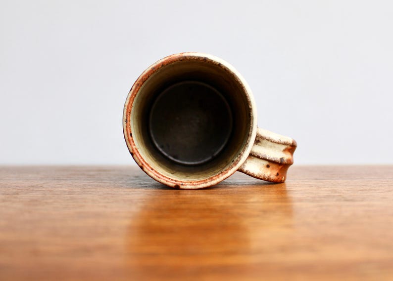 May include: A ceramic mug with a white glaze and brown and orange speckles. The mug has a rounded shape and a handle.