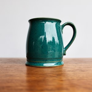 May include: A teal blue ceramic mug with a speckled glaze. The mug has a rounded body and a wide handle.