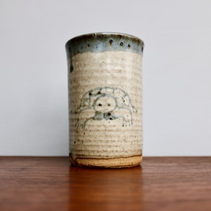May include: A white ceramic mug with a blue and brown rim. The mug has a simple drawing of a turtle on the front.