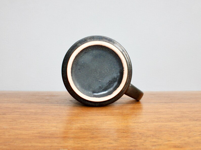 Pu&ograve; includere: Una tazza in ceramica grigio scuro con un bordo marrone chiaro. La tazza &egrave; appoggiata su una superficie di legno.