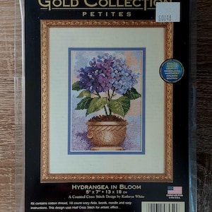 May include: A counted cross stitch kit titled Hydrangea in Bloom from The Gold Collection Petites. The packaging features a floral design of blue and purple hydrangea flowers in a tan pot, measuring 5 inches by 7 inches, with cotton thread.