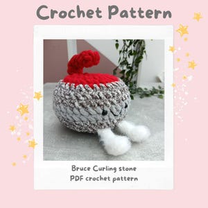 Puede incluir: Una piedra de curling de ganchillo con un asa roja y un cuerpo gris y blanco. La piedra tiene una cara sonriente y pies blancos. La imagen incluye el texto "Crochet Pattern" y "Bruce Curling stone PDF crochet pattern."