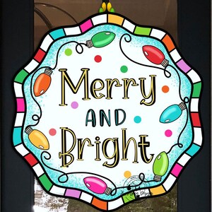 May include: A colorful wreath with a blue background and a white border. The wreath has a string of colorful lights and the words "Merry and Bright" in gold letters.
