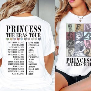 May include: White t-shirt featuring the text "PRINCESS THE ERAS TOUR" with a list of dates and princess names. The front of the shirt displays a grid of princess illustrations. A stylish and comfortable tee for fans of Disney princesses.