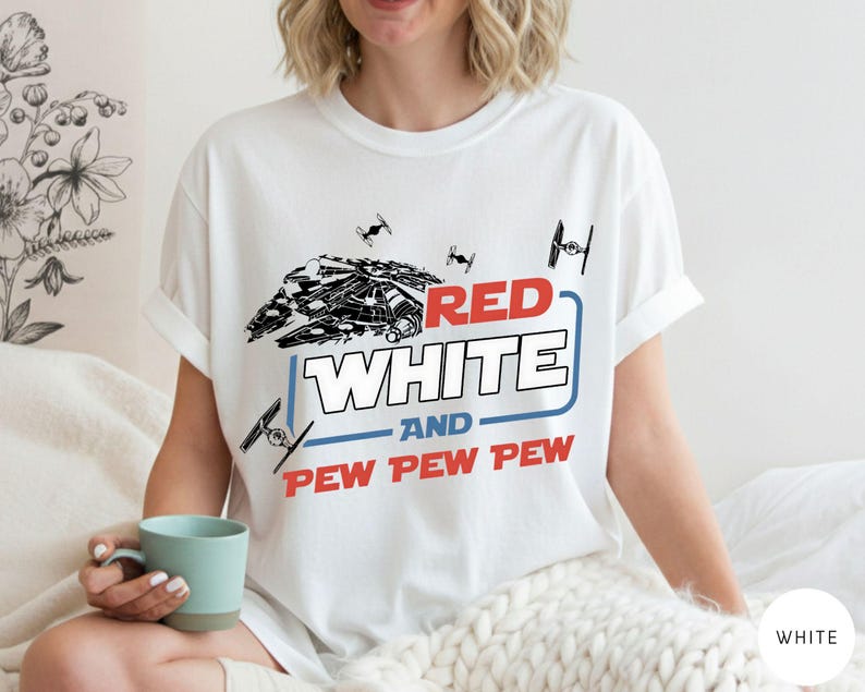 May include: A white short-sleeved t-shirt featuring a graphic of a spaceship and TIE fighters. The text reads RED WHITE AND PEW PEW PEW in red, white, and blue colors. The design includes a blue rectangular outline surrounding the word WHITE.