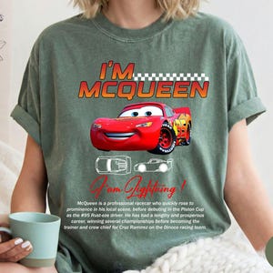 Puede incluir: Una camiseta verde musgo con un gr&aacute;fico de Rayo McQueen de la pel&iacute;cula Cars. El dise&ntilde;o incluye el texto "I'M MCQUEEN" y "I am Lightning!" con una imagen detallada del coche de carreras rojo. La camiseta tambi&eacute;n tiene una descripci&oacute;n del personaje.