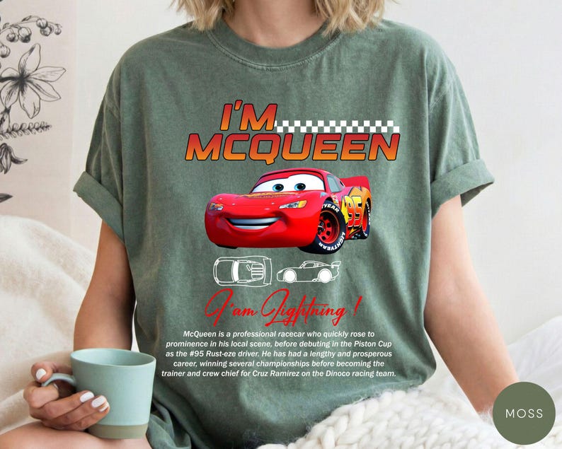 Puede incluir: Una camiseta verde musgo con un gr&aacute;fico de Rayo McQueen de la pel&iacute;cula Cars. El dise&ntilde;o incluye el texto "I'M MCQUEEN" y "I am Lightning!" con una imagen detallada del coche de carreras rojo. La camiseta tambi&eacute;n tiene una descripci&oacute;n del personaje.