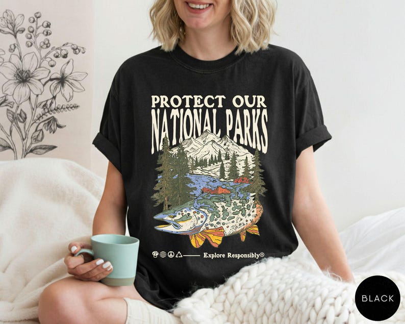 May include: Black t-shirt with a graphic that reads "PROTECT OUR NATIONAL PARKS." The graphic features a mountain range, trees, a lake, and a fish. The shirt also has the text "Explore Responsibly&reg;".