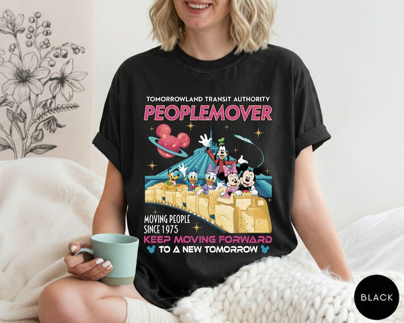 May include: Black t-shirt featuring a colorful graphic of the Tomorrowland Transit Authority PeopleMover ride with Mickey Mouse, Minnie Mouse, Goofy, Donald Duck, and Daisy Duck. The shirt includes the text "PEOPLEMOVER" and "KEEP MOVING FORWARD TO A NEW TOMORROW."