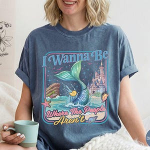 May include: Blue jean-colored t-shirt with a mermaid graphic. The graphic features a mermaid with a teal tail, a castle, and the text "I Wanna Be Where The People Aren't."