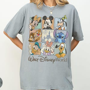 Może przedstawiać: Jasnoniebieska koszulka z nadrukiem przedstawiającym postacie Disneya, w tym Myszka Miki, Myszka Minnie, Goofy, Kaczor Donald, Kaczka Daisy, Pluto, Chip i Dale oraz Stitch. Pod spodem napis "Walt Disney World".