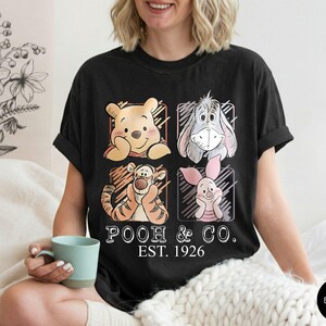 May include: Black t-shirt featuring Winnie the Pooh, Eeyore, Tigger, and Piglet. The shirt has the text "POOH & CO. EST. 1926" in a vintage style. The shirt is a comfortable, casual wear item.