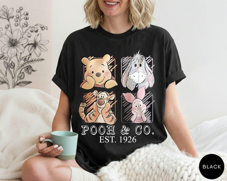 May include: Black t-shirt featuring Winnie the Pooh, Eeyore, Tigger, and Piglet. The shirt has the text "POOH & CO. EST. 1926" in a vintage style. The shirt is a comfortable, casual wear item.