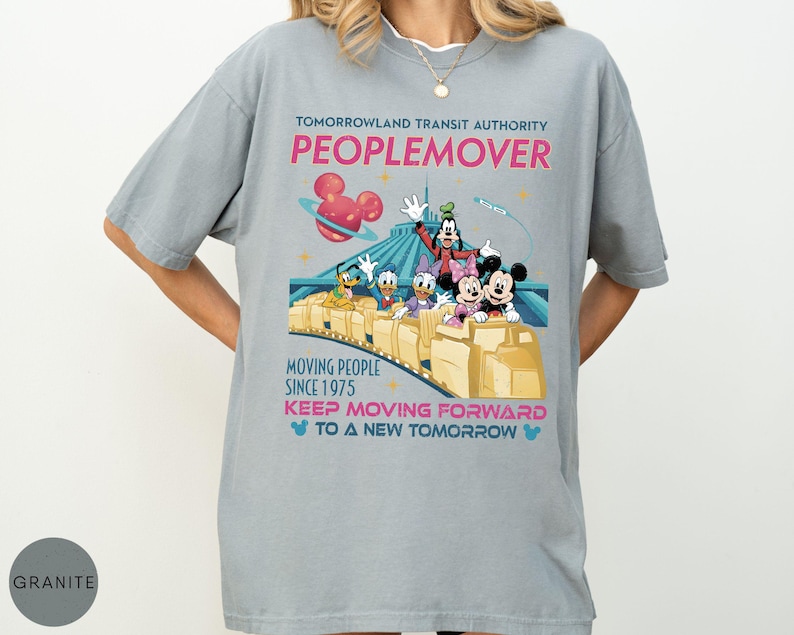 May include: A light gray t-shirt featuring the Tomorrowland Transit Authority Peoplemover ride with Disney characters. The design includes the text "MOVING PEOPLE SINCE 1975" and "KEEP MOVING FORWARD TO A NEW TOMORROW".