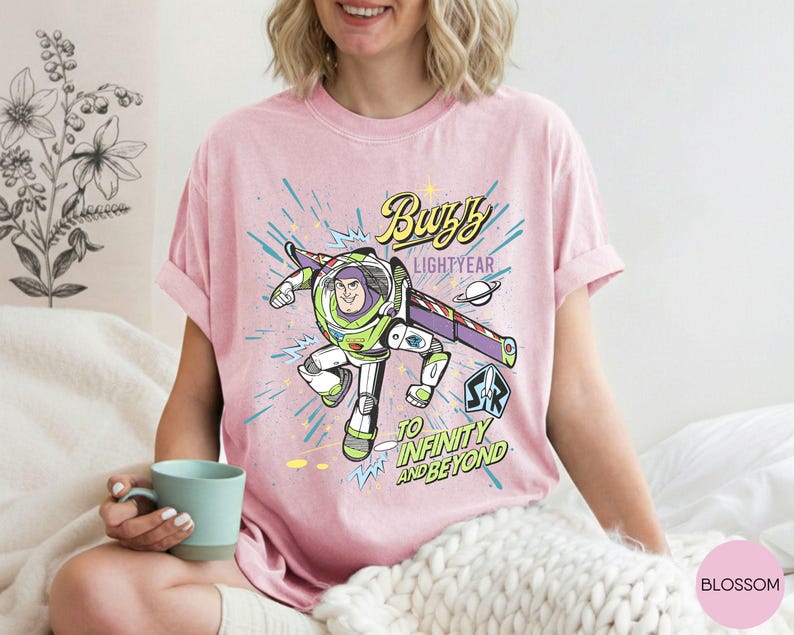 Peut inclure: T-shirt rose clair avec un graphisme de Buzz l'&Eacute;clair, le texte "Buzz Lightyear" et "To Infinity and Beyond". Le design comprend un th&egrave;me spatial avec une plan&egrave;te et des &eacute;toiles.