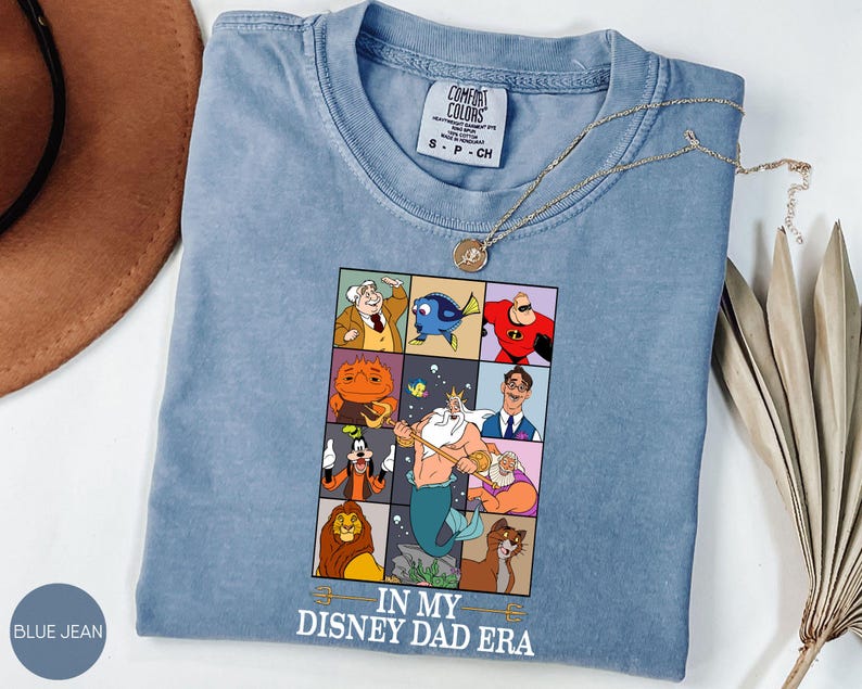 May include: Blue jean Comfort Colors t-shirt with a graphic featuring Disney characters in a grid. The graphic includes characters like Mr. Incredible, Dory, and King Triton. The text "IN MY DISNEY DAD ERA" is printed below the grid.