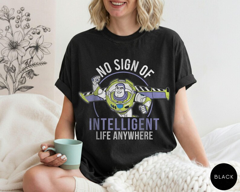 Puede incluir: Camiseta negra con un dise&ntilde;o de dibujos animados de Buzz Lightyear y el texto "NO SIGN OF INTELLIGENT LIFE ANYWHERE" en blanco y morado. Una prenda c&oacute;moda y casual.