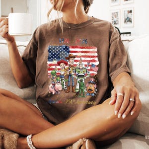Pu&ograve; includere: T-shirt color espresso con grafica dei personaggi di Toy Story davanti a una bandiera americana con la scritta "1776-2026" e "America - 250th Anniversary". La maglietta ha una vestibilit&agrave; rilassata.