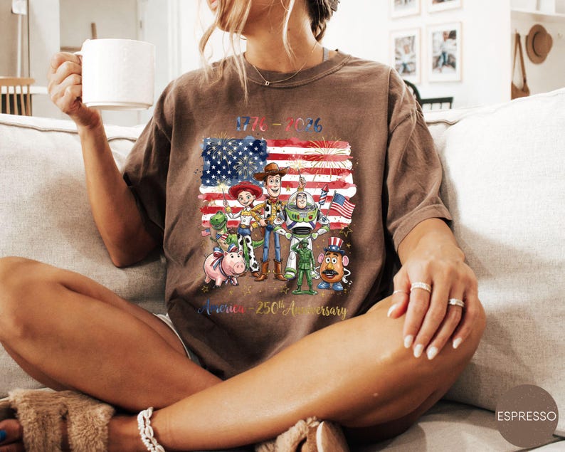 Pu&ograve; includere: T-shirt color espresso con grafica dei personaggi di Toy Story davanti a una bandiera americana con la scritta "1776-2026" e "America - 250th Anniversary". La maglietta ha una vestibilit&agrave; rilassata.