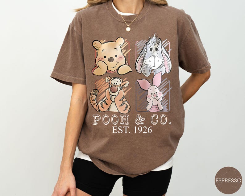 May include: Brown t-shirt featuring Winnie the Pooh, Eeyore, Tigger, and Piglet. The shirt has the text "POOH & CO. EST. 1926" in a vintage style. The shirt is a relaxed fit and has a crew neck.