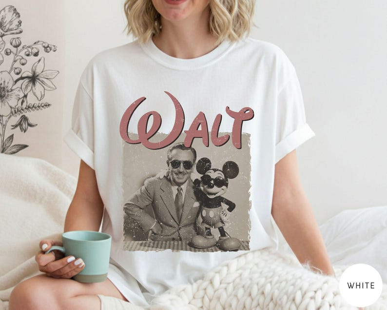 Puede incluir: Camiseta blanca con una imagen retro de Walt Disney y Mickey Mouse con gafas de sol. La palabra "Walt" est&aacute; impresa encima de la imagen en una fuente rosa vintage. La camiseta es de estilo cuello redondo cl&aacute;sico.