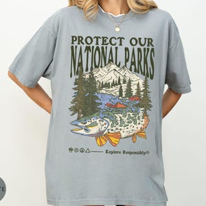 May include: A light blue t-shirt with the text "PROTECT OUR NATIONAL PARKS" above a graphic of a mountain range, trees, and a fish. The phrase "Explore Responsibly" is below the graphic.