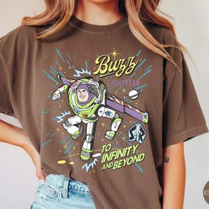 Peut inclure: Une tasse en c&eacute;ramique blanche avec une anse noire et l'inscription "But First, Coffee" en gras noir. La tasse contient un liquide fonc&eacute;, probablement du caf&eacute;, et repose sur une surface claire.