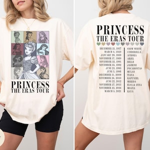 May include: Ivory-colored t-shirt featuring a graphic of Disney princesses in a grid, with the text "PRINCESS THE ERAS TOUR." The back of the shirt lists dates and princess names. A casual, oversized fit.