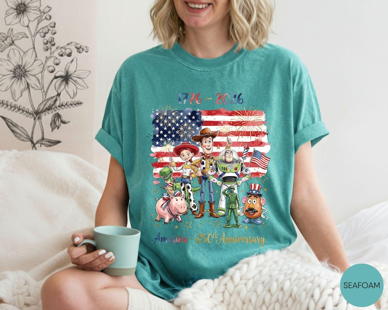 Pu&ograve; includere: T-shirt color verde acqua con grafica dei personaggi di Toy Story davanti a una bandiera americana con fuochi d'artificio. Il testo recita "1776-2016" e "America 250th Anniversary". La maglietta &egrave; in stile casual e confortevole.