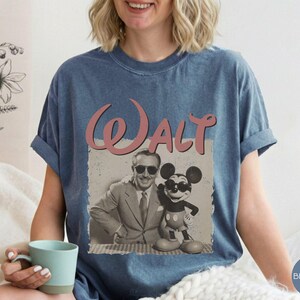 Puede incluir: Camiseta azul vaquero con un gr&aacute;fico de estilo vintage de Walt Disney con Mickey Mouse. La palabra "Walt" est&aacute; en escritura rosa encima de la imagen. La camiseta tiene las mangas enrolladas.