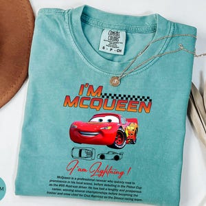 Puede incluir: Camiseta verde mar con un dise&ntilde;o de Rayo McQueen de la pel&iacute;cula Cars. La camiseta muestra el texto "I'm McQueen" y "I'm Lightning!". Un collar dorado est&aacute; colocado sobre la camiseta. Talla S-P-CH.