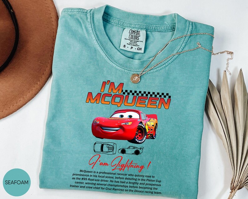 Puede incluir: Camiseta verde mar con un dise&ntilde;o de Rayo McQueen de la pel&iacute;cula Cars. La camiseta muestra el texto "I'm McQueen" y "I'm Lightning!". Un collar dorado est&aacute; colocado sobre la camiseta. Talla S-P-CH.