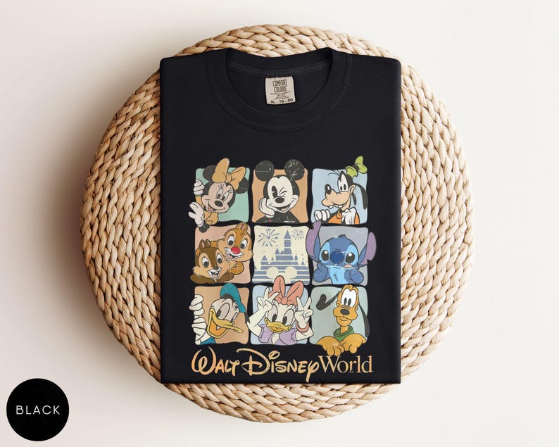 Może przedstawiać: Czarny t-shirt z kolorową siatką postaci Disneya, w tym Myszki Miki, Myszki Minnie, Goofy'ego i Stitcha. Słowa "Walt Disney World" są wydrukowane złotym pismem pod siatką. Koszulka jest złożona na tkanej powierzchni.