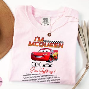 Puede incluir: Camiseta rosa claro con un gr&aacute;fico de Rayo McQueen de la pel&iacute;cula Cars. La camiseta muestra el texto "I'M MCQUEEN" y "I am Lightning!". Tambi&eacute;n hay una descripci&oacute;n del personaje en la camiseta.