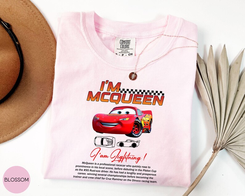 Puede incluir: Camiseta rosa claro con un gr&aacute;fico de Rayo McQueen de la pel&iacute;cula Cars. La camiseta muestra el texto "I'M MCQUEEN" y "I am Lightning!". Tambi&eacute;n hay una descripci&oacute;n del personaje en la camiseta.