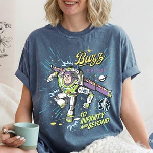 Peut inclure: T-shirt bleu jean avec un motif de Buzz l'&Eacute;clair de Toy Story. Le design comprend le texte "Buzz Lightyear" et "To Infinity and Beyond" avec une image de dessin anim&eacute; du personnage en combinaison spatiale.