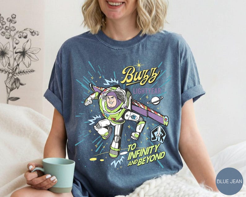 Peut inclure: T-shirt bleu jean avec un motif de Buzz l'&Eacute;clair de Toy Story. Le design comprend le texte "Buzz Lightyear" et "To Infinity and Beyond" avec une image de dessin anim&eacute; du personnage en combinaison spatiale.