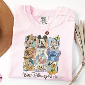 Może przedstawiać: Jasnor&oacute;żowa koszulka z kolorową grafiką postaci Disneya w kwadratowych ramkach. Koszulka zawiera Myszkę Miki, Minnie, Goofy'ego, Chipa i Dale'a, Stitcha, Kaczora Donalda, Daisy Duck i Pluto. Tekst "Walt Disney World" jest wydrukowany poniżej.