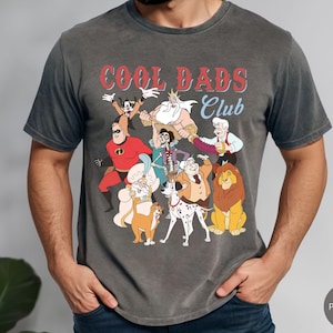 May include: Dark gray t-shirt featuring a graphic of cartoon characters with the text "COOL DADS Club" in red and blue. The shirt has a vintage, faded look and a crew neck.