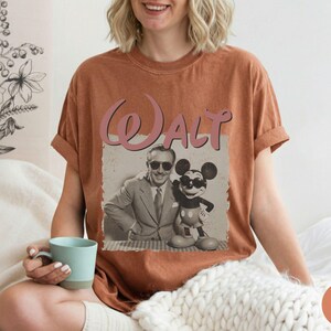 Puede incluir: Una camiseta de color &oacute;xido con un gr&aacute;fico de estilo vintage de Walt Disney y Mickey Mouse. La palabra "Walt" est&aacute; impresa encima de la imagen en rosa, en cursiva. La camiseta tiene mangas cortas y un corte holgado.