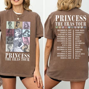 May include: Espresso-colored t-shirt featuring a graphic of Disney princesses and the text "PRINCESS THE ERAS TOUR." The front displays princess portraits. The back lists princess names and tour dates. A casual, comfortable tee.