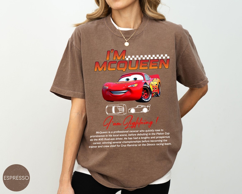 Puede incluir: Camiseta marr&oacute;n con el texto "I'M MCQUEEN" y un gr&aacute;fico de un coche de carreras rojo. La camiseta tambi&eacute;n incluye el texto "I am Lightning!" y una descripci&oacute;n del personaje. La camiseta es de corte holgado.