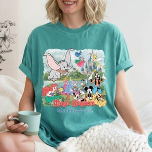 May include: A seafoam green short-sleeve t-shirt featuring a graphic print of Dumbo, Mickey Mouse, and other Disney characters in front of a castle. The text Magic Kingdom and Walt Disney World is printed in red and blue below the characters.