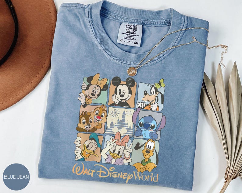 Może przedstawiać: Niebieska koszulka dżinsowa z kolorową grafiką postaci Disneya, w tym Myszki Miki i Myszki Minnie. Koszulka ma okrągły dekolt i kr&oacute;tkie rękawy. U dołu nadrukowano napis "Walt Disney World".