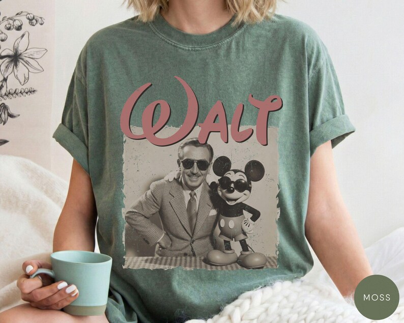 Puede incluir: Camiseta verde musgo con un gr&aacute;fico vintage de Walt Disney y Mickey Mouse. La palabra "Walt" est&aacute; escrita en rosa sobre la imagen. La camiseta tiene mangas cortas y cuello redondo.